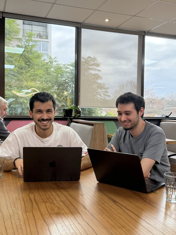 Two colleagues smiling over their laptops in front of a large window